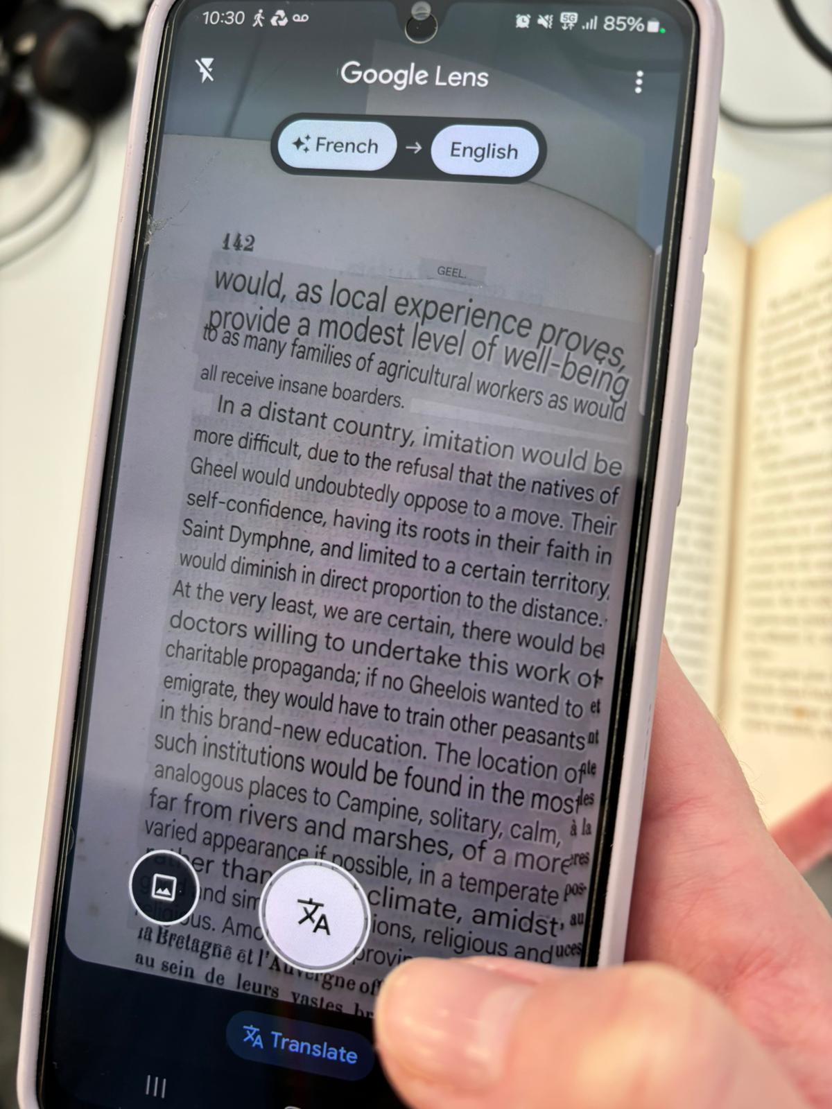 A smart phone held over a book. The phone screen shows the book through the camera (Google Lens) but the text is translated. 